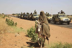 FILE - In this Nov. 20, 2014 file photo taken on a government organized media tour, a woman rides a donkey past a convoy of government troops in Tabit village in the North Darfur region of Sudan, where allegations surfaced of rape of women by government allied troops. In January 2019, Al-Bashir is facing a tough challenge to his grip on power as street protests show no sign of abating. In the 2000s, Sudan was most known for the brutal repression of an uprising in its western Darfur region, when the pro-government militias known as the Janjaweed became notorious for atrocities and al-Bashir himself was indicted by the International Criminal Court for alleged war crimes and genocide.