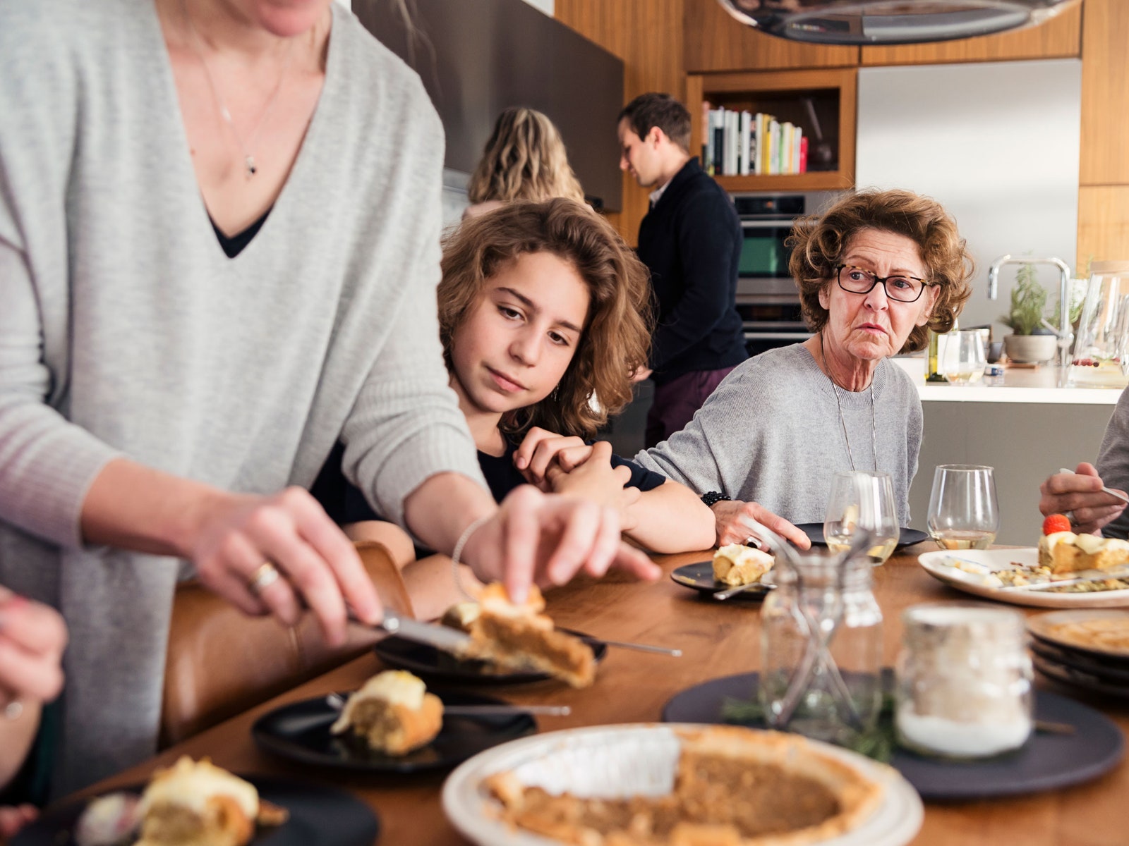 An older woman and a young girl watch as another woman slices a pie.