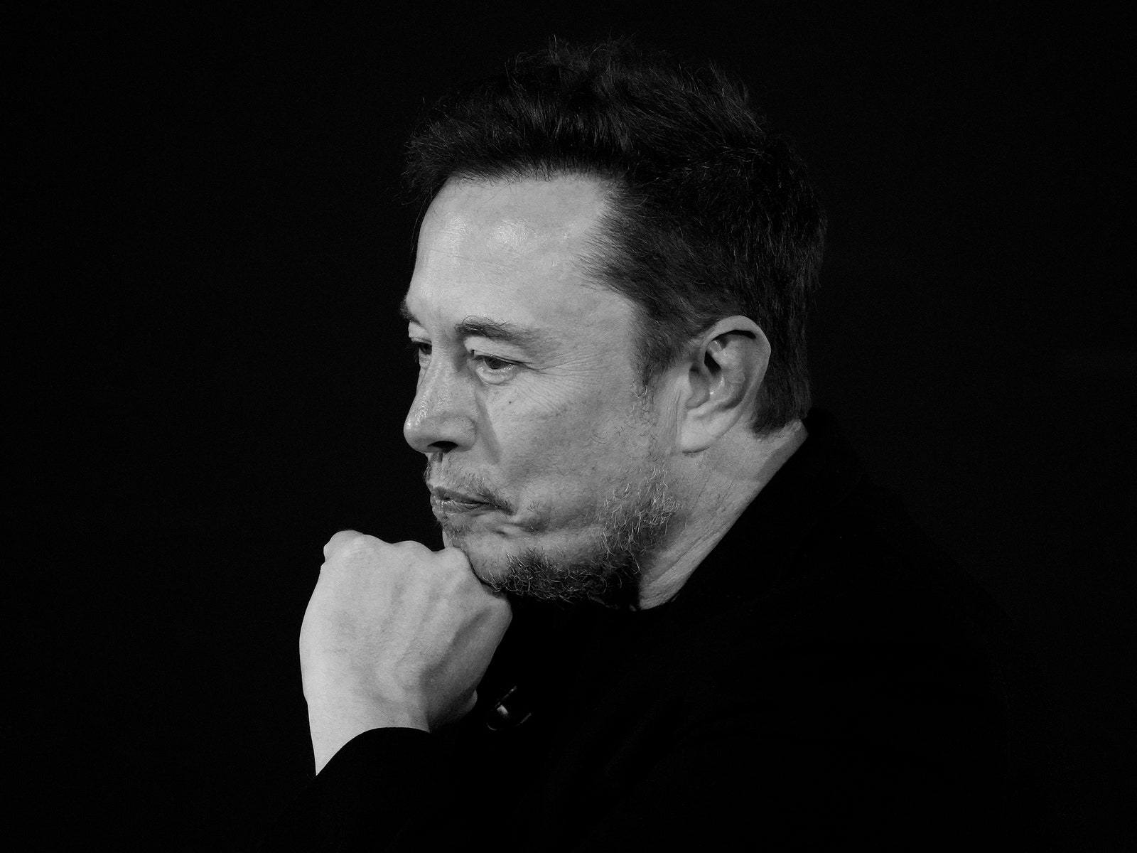 Black and white photograph of Elon Musk holding his left hand near his face