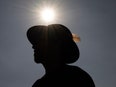 A person standing outside with the sun above them, they wear a hat with a feather sticking out