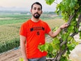 Writer Mosab Abu Toha stands next to a plant wearing gray pants and a bright orange shirt