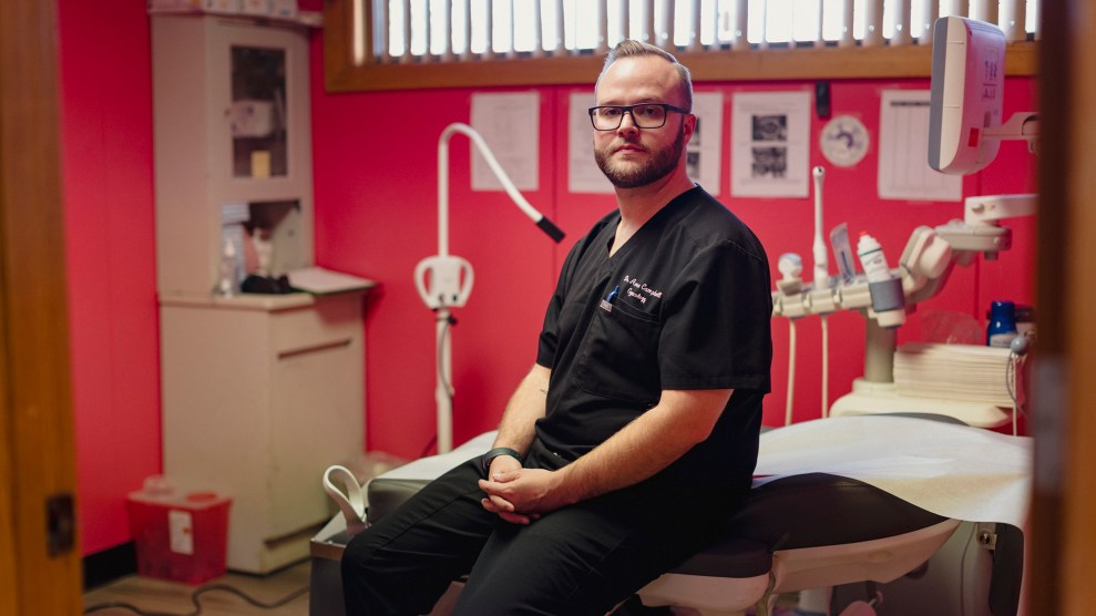 Doctor with glasses sitting in a red-walled medical facility.