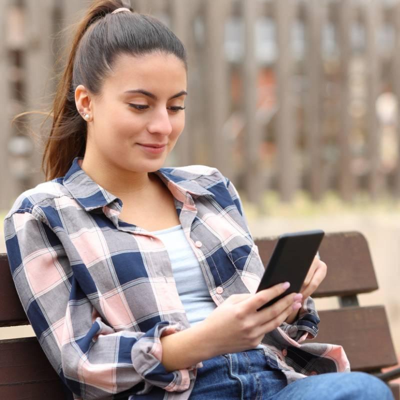 A woman scrolling on her cellphone while sitting on a park bench.