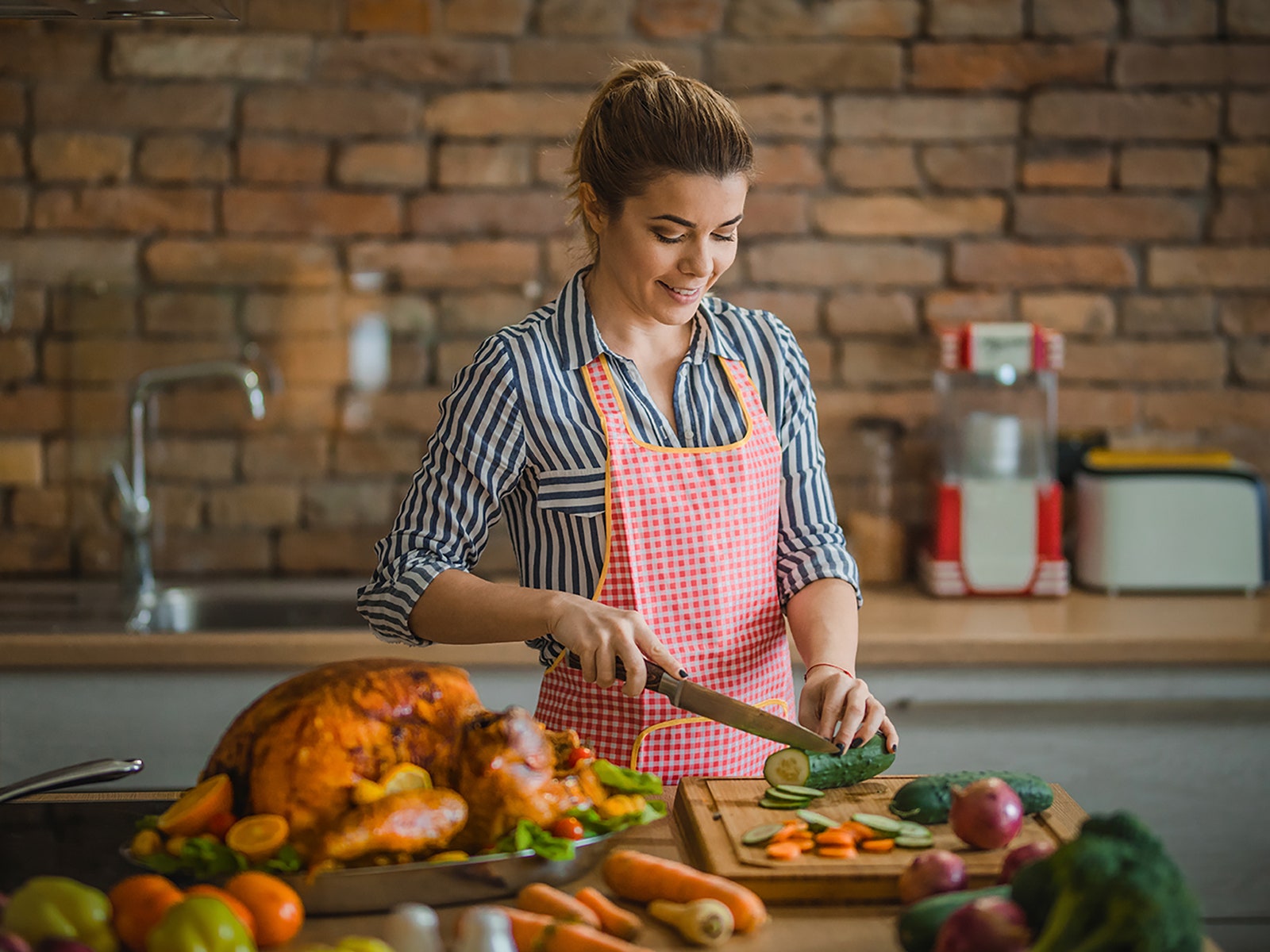 Person wearing apron chops vegetable on cutting board with Thanksgiving Turkey on the counter