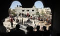 Palestinians search in rubble of destroyed building, seen through large hole in wall of another building with people's heads silhouetted against the light