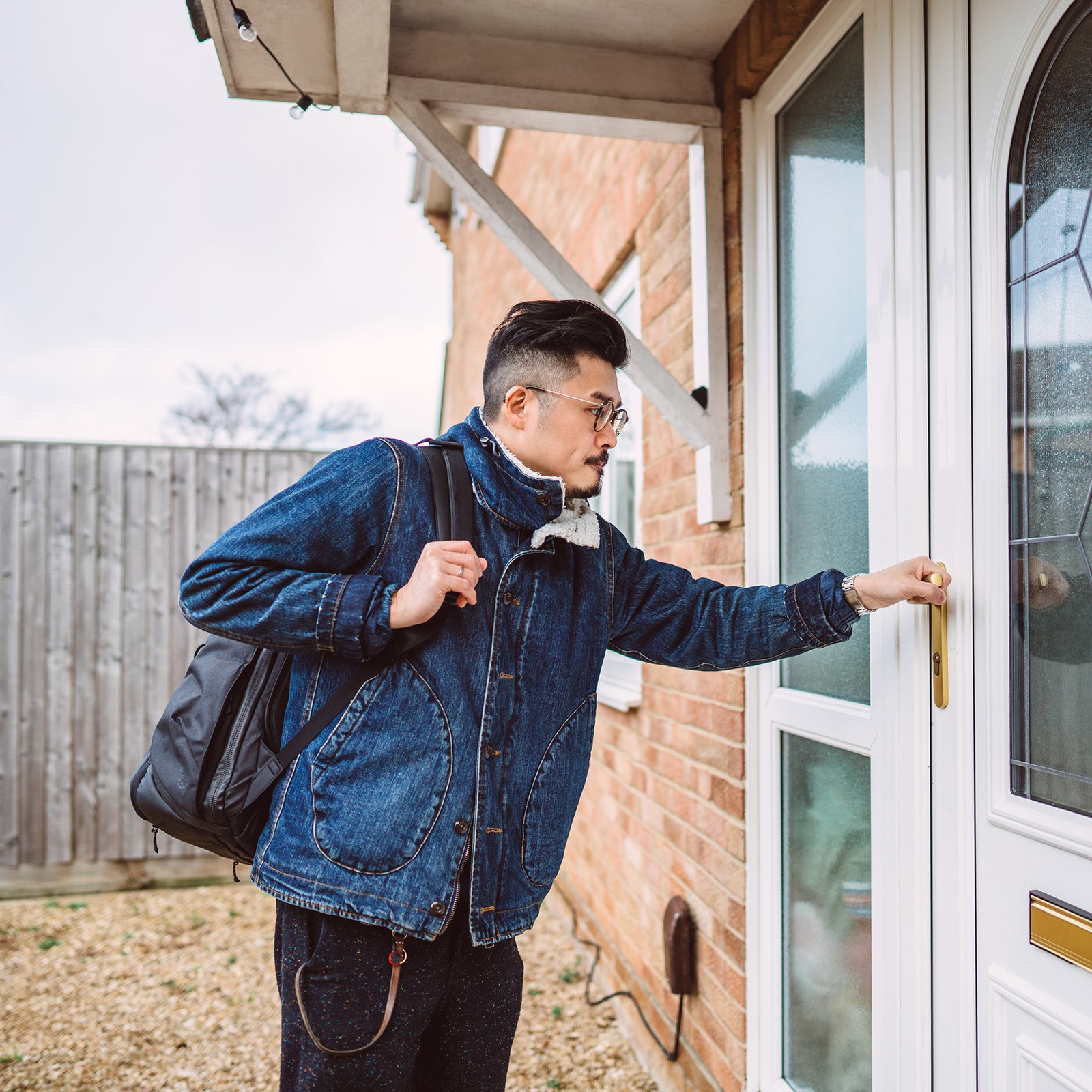 Young man with a backpack opening the front door of his house.