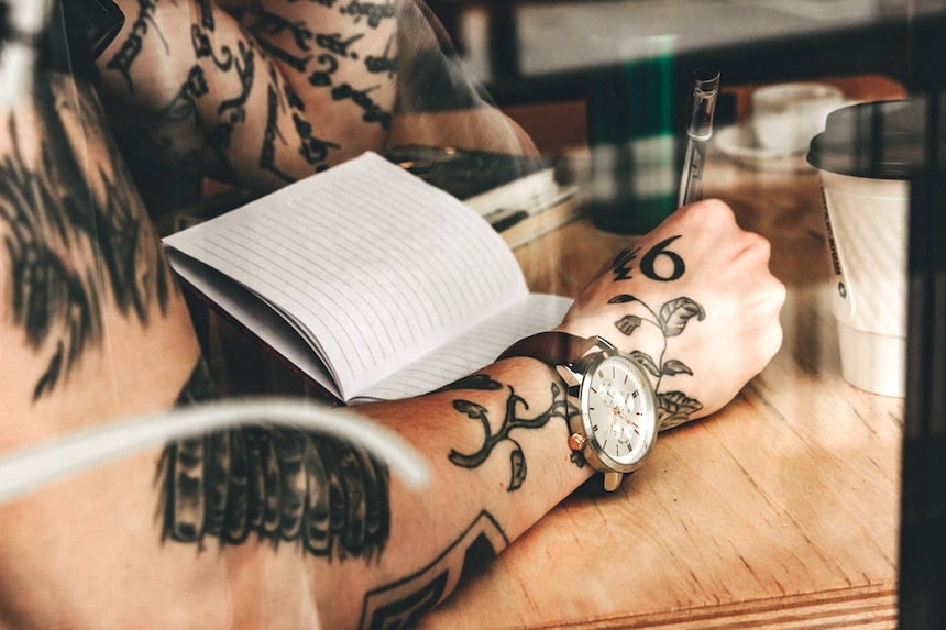 Tattooed person writing in a notebook in a cafe. (Photo by Eric Didier.)