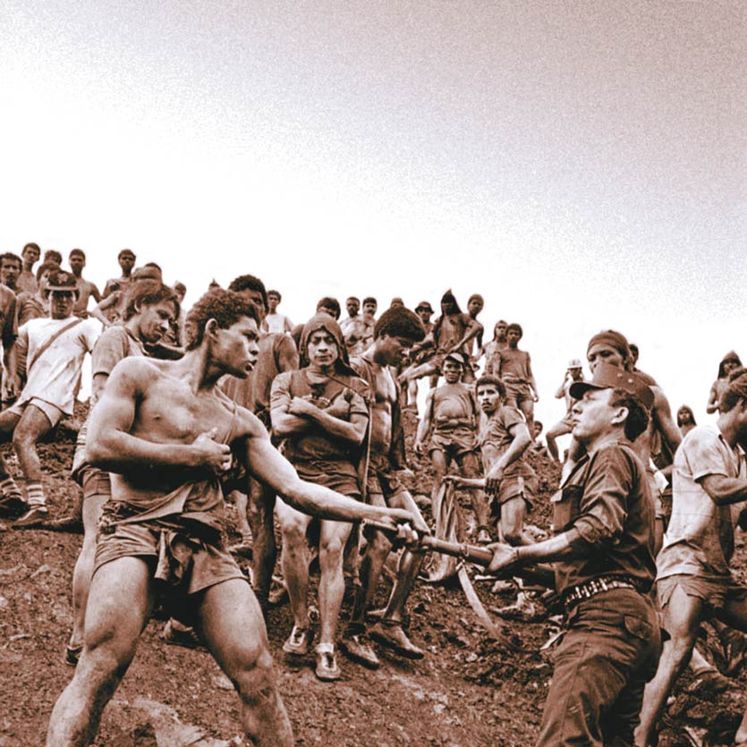 a worker in a gold mine confronts soldier keeping guard and grabs his rifle by the barrel as a crowd of workers watch