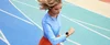 A woman wearing a blue top and orange shorts looks at Google Pixel Watch 2 on her wrist. She is running on a multi-colored track.