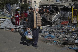 Palestinians walk by destroyed buildings in Rafah, Gaza Strip, Thursday, Nov. 30, 2023, during a temporary ceasefire between Israel and Hamas.