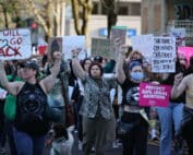 A crowd of people march in the street to protest the leak of a Supreme Court ruling overturning Roe V. Wade. They are raising their fists and holding signs.