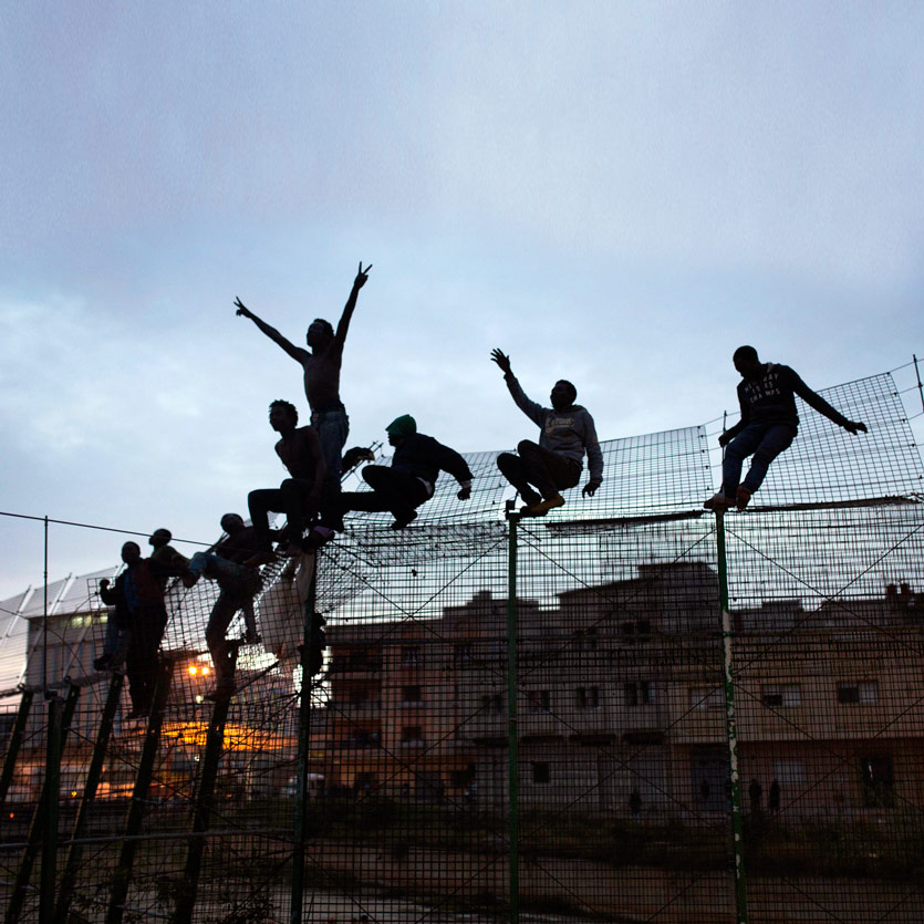 a grouple of people sits upon a tall boundary fence they have climbed