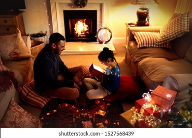 Side view of a mixed race man sitting on the floor with his young daughter in their sitting room at Christmas, smiling and giving a present Stock Photo