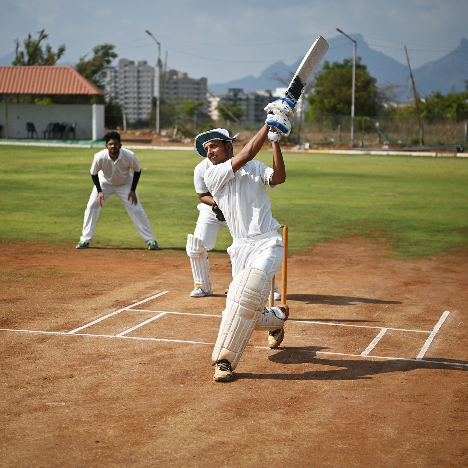 A person swinging a cricket bat two people stand behind them.