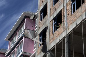 File - In this Thursday, Oct. 17, 2013 photo, a woman directs a loaded cement crane on a residential building under construction in Xiahe, Gansu Province, China. An earthquake in Gansu province has killed at least 118 people.