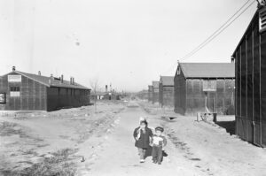 Two small children walking down a dirt path between barracks at Minidoka.