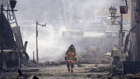 A firefighter looks up the rubble and wreckage of a burnt-out marketplace following an earthquake in Wajima.