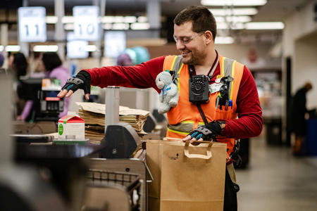 A worker in a hi-viz vest bags grocery at checkout.