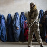 A Taliban fighter stands guard as women wait to receive food rations, in Kabul, Afghanistan, last year.