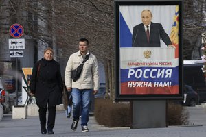 FILE - People walk past a billboard with an image of Russian President Vladimir Putin and words reading "The West doesn't need Russia, we need Russia!" in a street in Sevastopol, Crimea, on March 6, 2024.