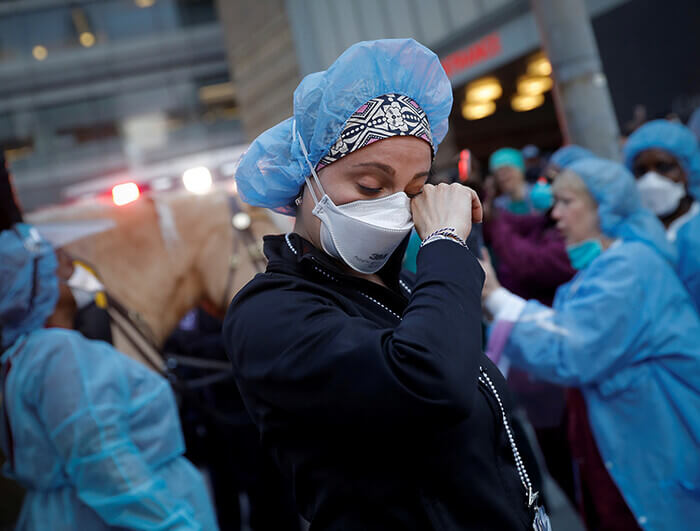 A nurse in a face mask wipes away a tear.