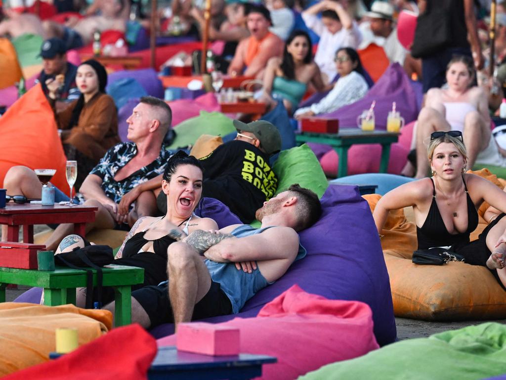 Foreign tourists relax on the Kuta Beach near Denpasar on Indonesia's resort island of Bali on November 18, 2023. (Photo by SONNY TUMBELAKA / AFP)