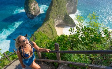 Young female tourist visiting Kelingking Beach on the Indonesian island of Nusa Penida. Climbs up the step trail to the top.