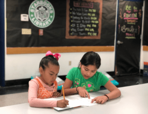 Two girls sitting at a table and writing.