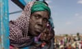 A woman wearing a headscarf looks out of the side of a truck packed with people