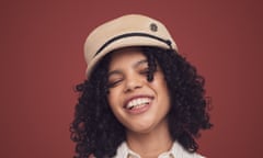 The model wears a soft beige oversize cap. She has black curly hair and is laughing.