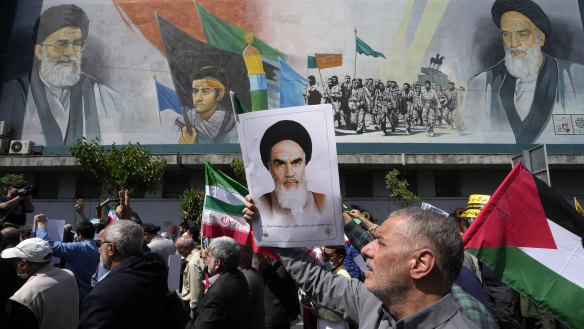 People walk past a mural showing Ayatollah Khomeini, right, Supreme Leader Ayatollah Ali Khamenei, left, while holding a poster of Ayatollah Khomeini and Iranian and Palestinian flags in an anti-Israeli march after Friday prayers in Tehran.