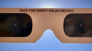 the sun can be seen through a pair of dark solar eclipse glasses held up to the sky