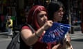 A woman fans herself as she and another woman walk across a street