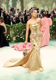 a woman in a gold gown standing on a white floor with cameras around her and people taking pictures