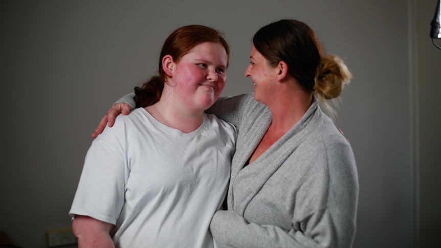 Mother smiles adoringly with her arm around her daughter as they look into each other's eyes.