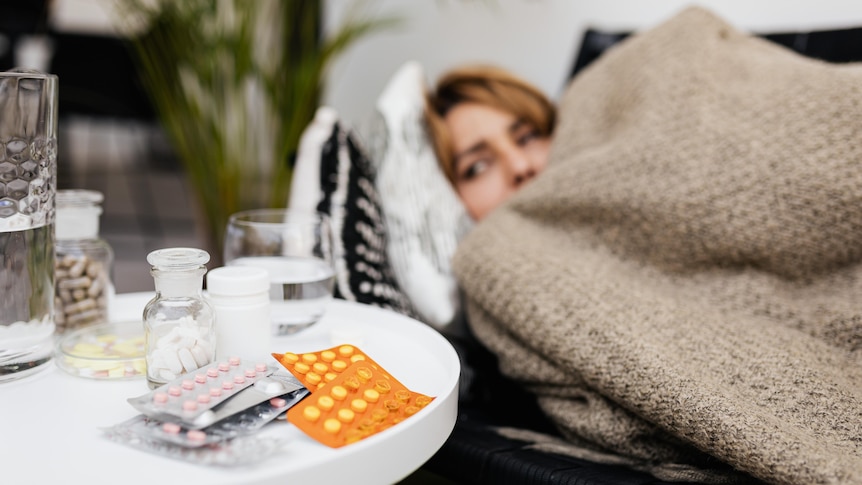 A woman lying in bed with medications next to her