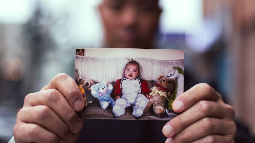 Luke Bowden stands outside the eastern Welfare Society adoption centre in Seoul, holding a photo of himself as a baby.