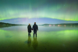 Sky’s the limit: this photo of two people watching the aurora australis light up a southern Tasmanian beach about 5am on Saturday was taken on a digital camera.