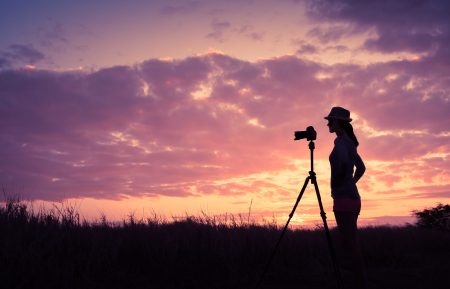 Silhouette of woman taking a photo with a camera on a tripod