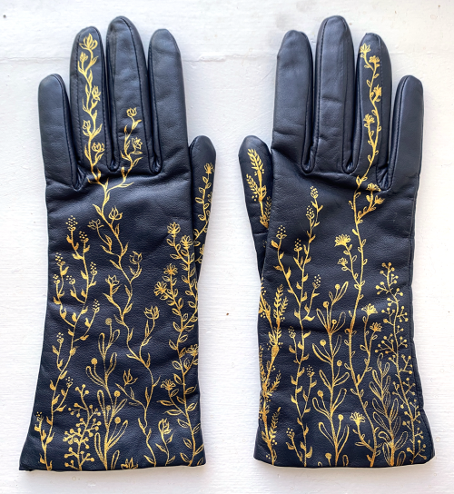 Photo of a pair of navy gloves that have vine-like floral elements painted on the backs up some of the fingers.