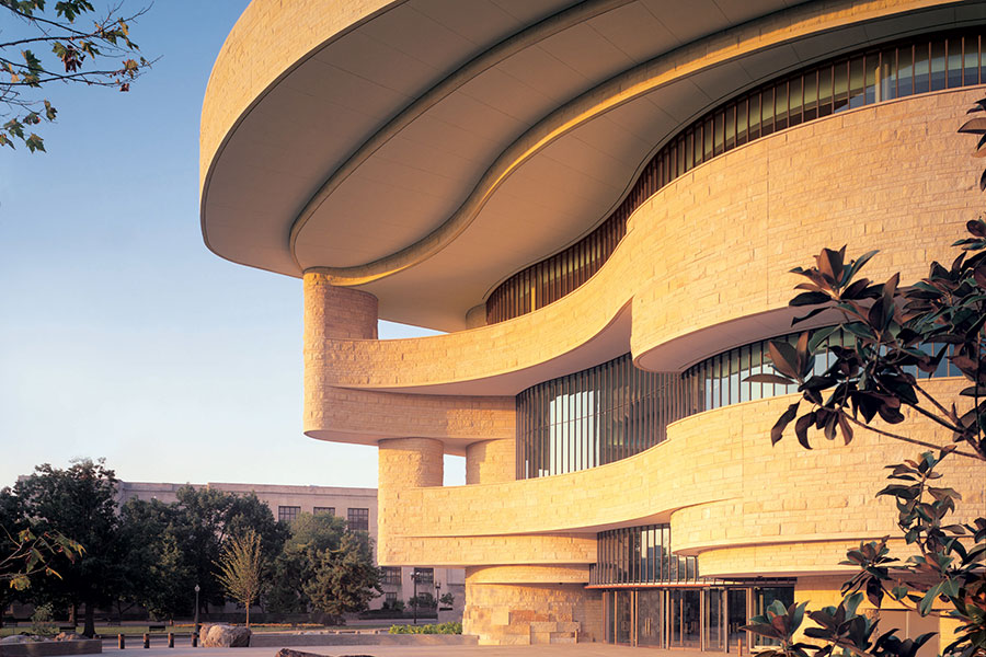 Curved exterior of the National Museum of the American Indian in DC, pale bricks glowing as if during sunrise.