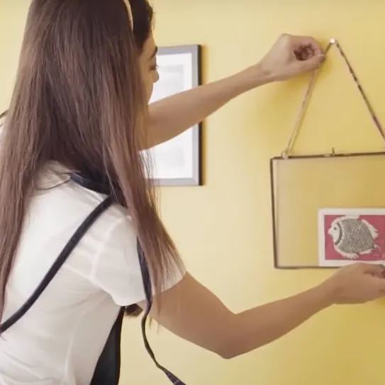 A woman hanging a decor on a yellow painted wall