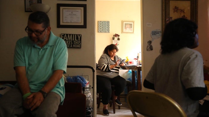 Marisol Coronado, center, prepares for a zoom call, while her husband and son spend time in the living room of their apartment in Huntington Park on April 19, 2024.