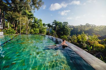 portrait of beautiful woman in luxurious resort. Young girl taking a bath and relaxing at infinity swimming pool