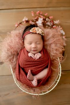 a newborn baby is wrapped in a red blanket and wearing a pink flower headband