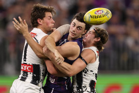 Jordan Clark of the Dockers handballs against Patrick Lipinski and Harvey Harrison of the Magpies.