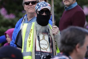 File - In this May 14, 2020, photo, a person caring a sign supporting QAnon wears a t-shirt that shows the QAnon name in the format of a rope noose during a protest rally in Olympia, Wash., held against Gov. Jay Inslee and Washington state stay-at-home orders made in efforts to prevent the spread of the coronavirus.