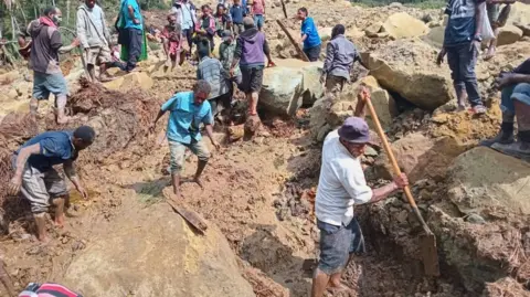 Villagers clamber over the landslide and use shovels to break up the earth