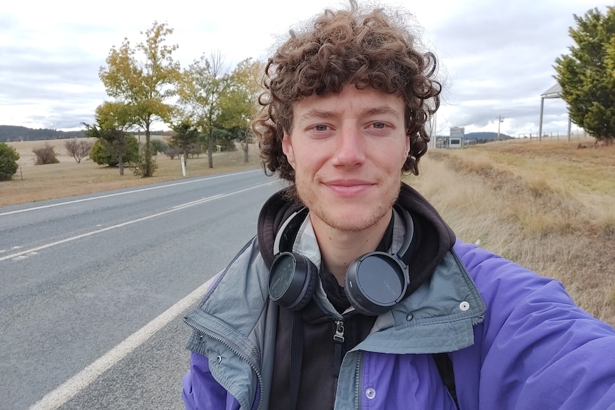 A man wearing a jacket and headphones walking on a highway.