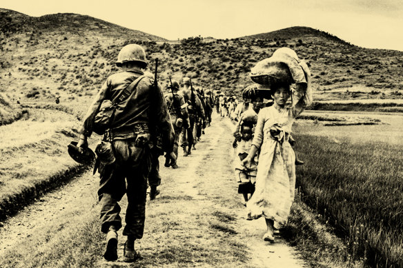 US soldiers file past Korean women and children carrying their possessions in 1950. 